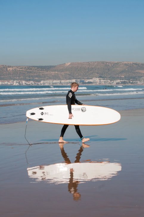 Man carrying beginner surfboard on beach